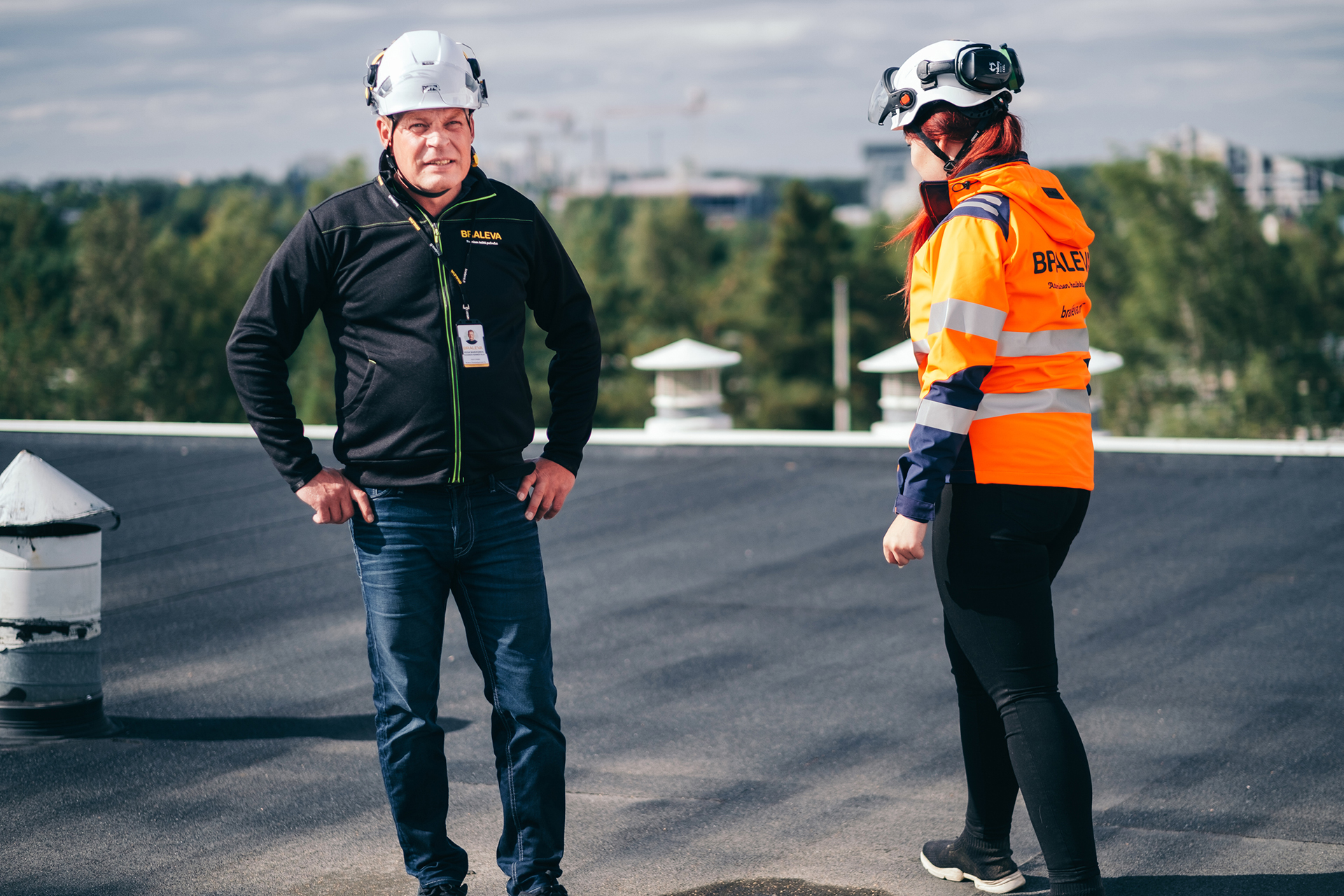 Kaksi Bralevan työntekijää turvakypärissä ja työvaatteissa seisoo talon katolla. Aurinko paistaa ja on kesä.